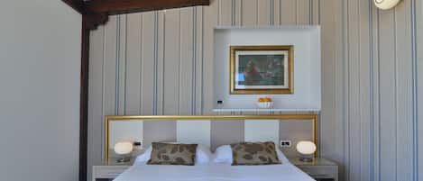 Quarto de hotel com uma cama grande, duas mesas de cabeceira, uma luminária de parede e um quadro emoldurado sobre a cama.
