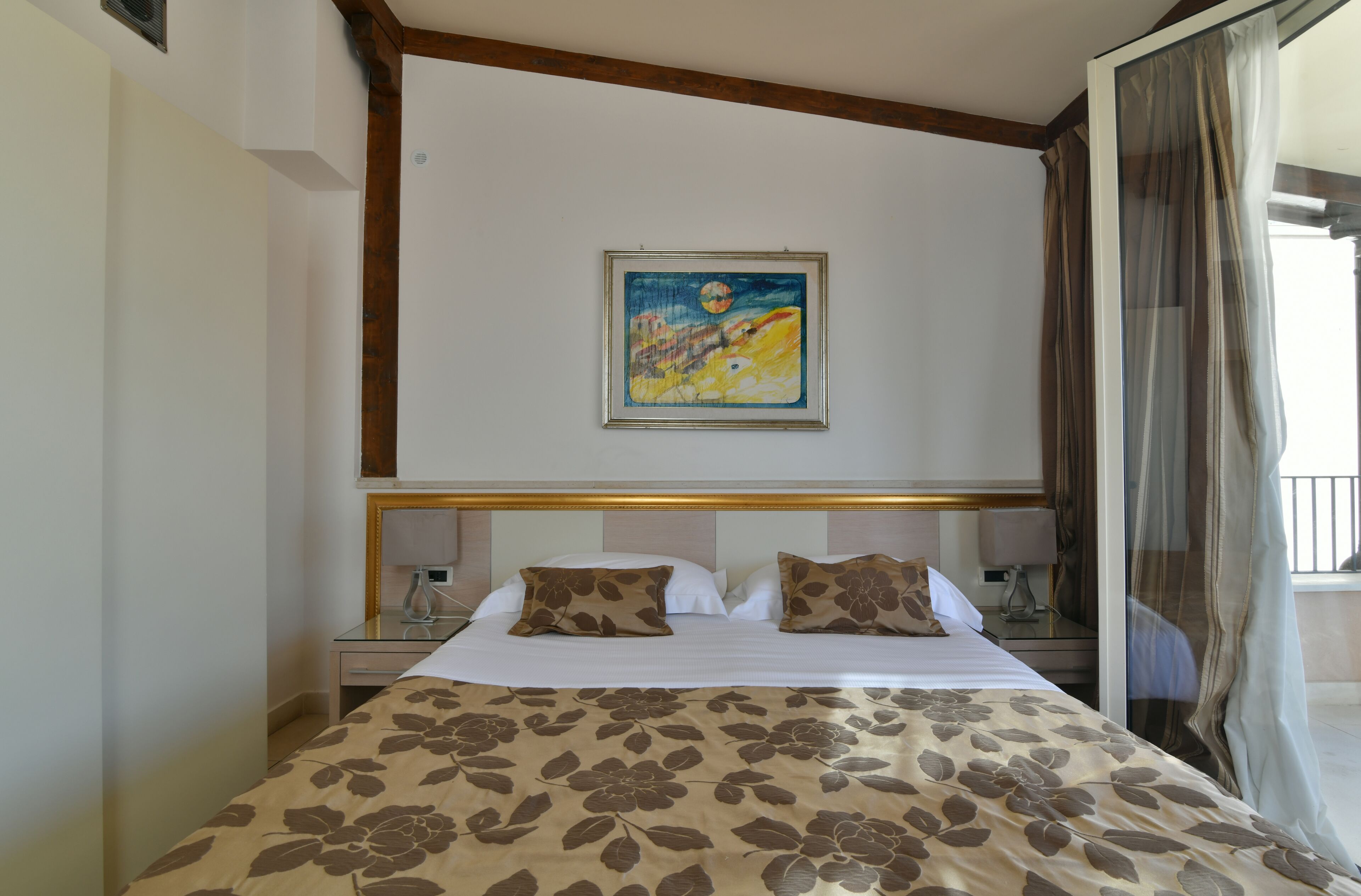 A hotel room with a large bed, a painting on the wall, and a view of the outdoors.