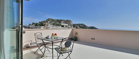 A balcony with a table and chairs, overlooking a cityscape with buildings and a hill.
