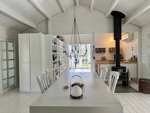 En matplats med ett långt bord, vita stolar, en kristallkrona, en bokhylla och ett kök med en spis.