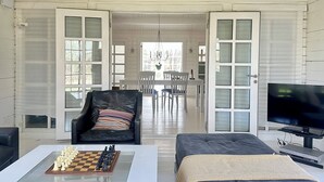 Un vaste salon comprenant un jeu d’échecs, un fauteuil en cuir, un canapé, un téléviseur et, au fond, un coin repas.