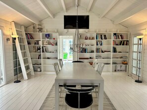 Ein Zimmer mit einem langen Tisch, Stühlen, Bücherregalen, einer Leiter und einem an der Decke befestigten Fernseher.