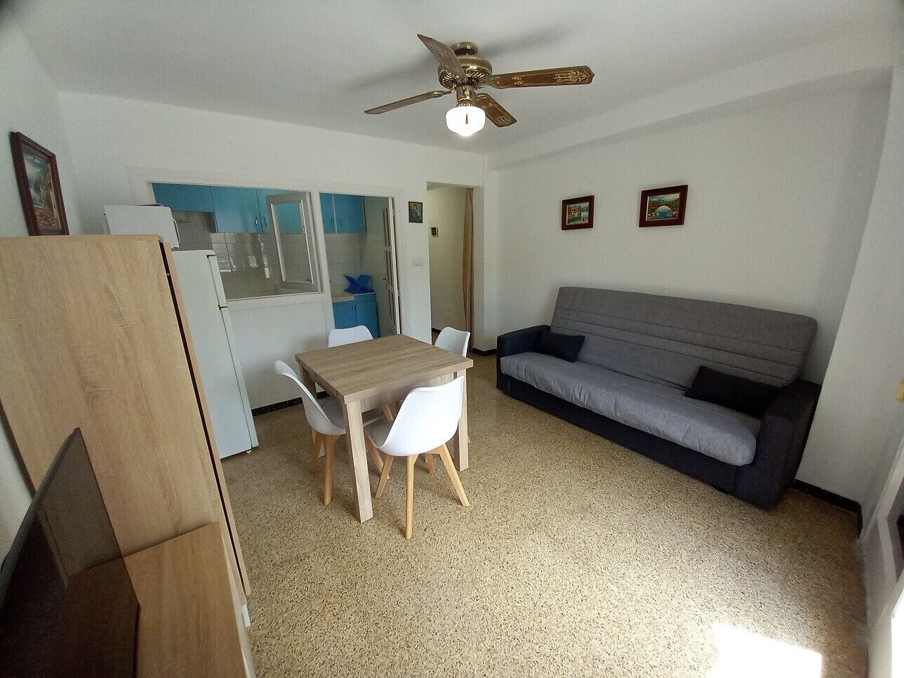 Un espace de vie compact comprenant un coin repas, un canapé, un ventilateur de plafond et une kitchenette.
