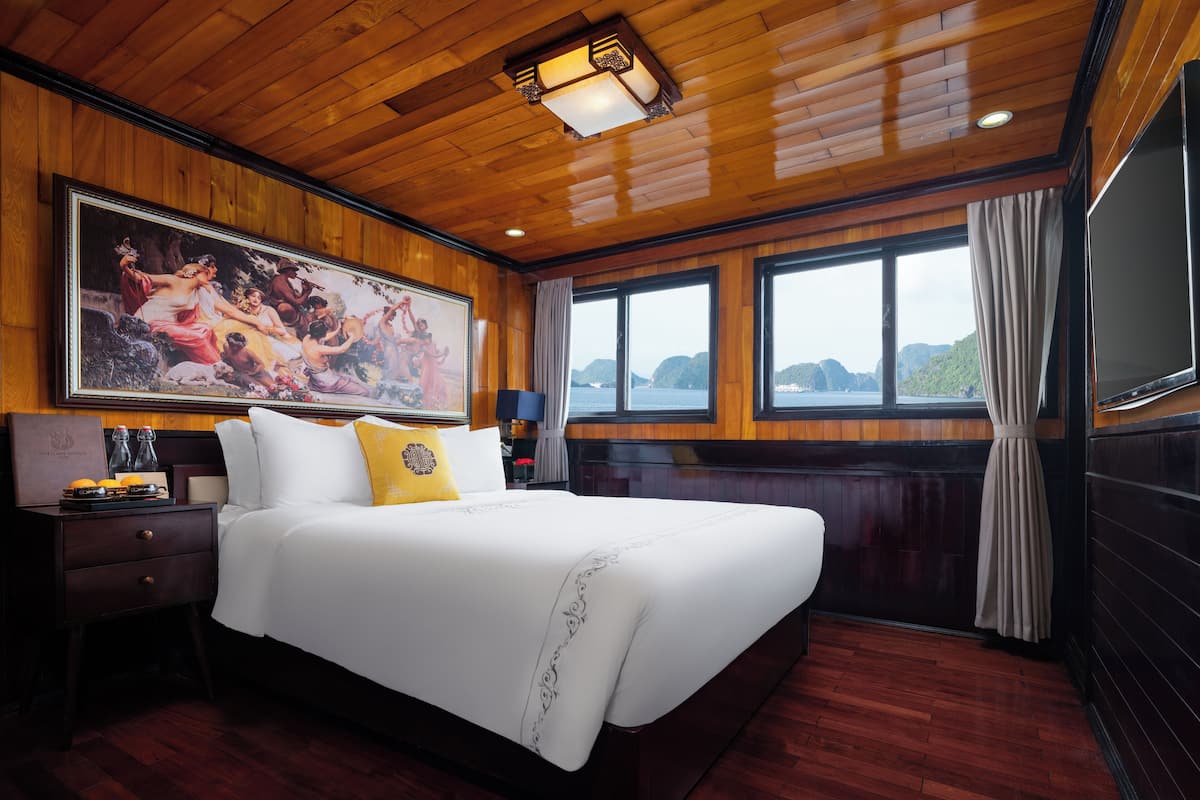 A large bed with white linens and a decorative pillow, a wooden ceiling, and a painting above the bed.