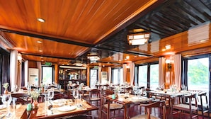 Un restaurante con techo y paredes de madera, mesas dispuestas con copas de vino, y vistas al exterior con vegetación.