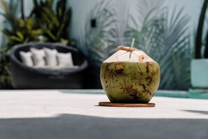 Une noix de coco rustique, dont la coque est usée par les intempéries, avec une paille, posée sur un sous-verre en bois.