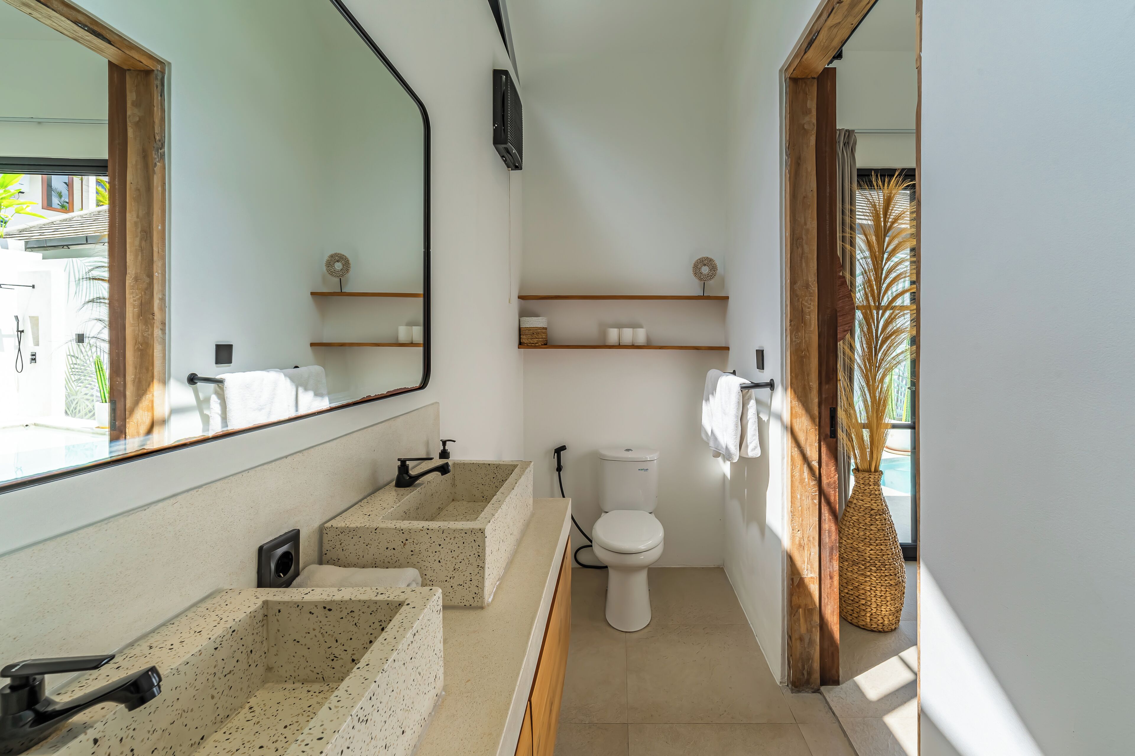 Een moderne badkamer met een grote spiegel, twee wasbakken, een toilet en houten planken.