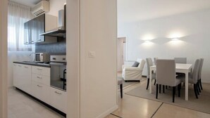 Een moderne keuken met witte kastjes en een eethoek met een witte tafel en stoelen.