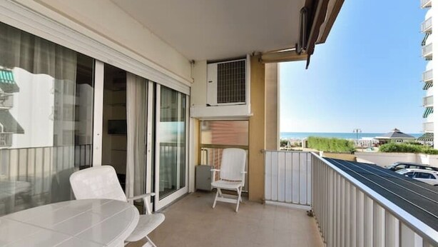 Een balkon met een tafel en stoelen, een schuifdeur en uitzicht op zee.
