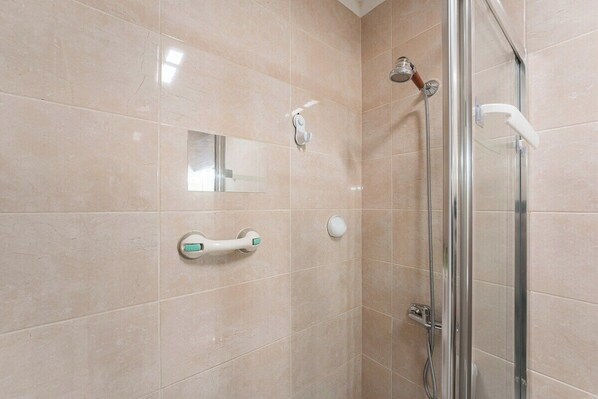 A modern bathroom with beige tiles, a glass shower enclosure, a handheld showerhead, a wall-mounted towel rack, and a mirror.