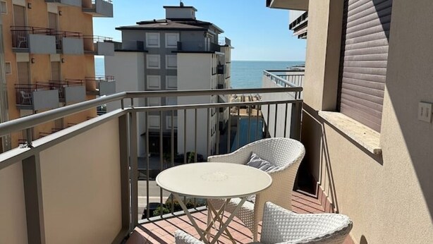 Un balcon avec une table et des chaises, donnant sur une étendue d’eau et des bâtiments.