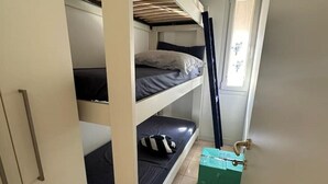 Une chambre de dortoir avec des lits superposés, une fenêtre et une valise verte posée sur le sol.