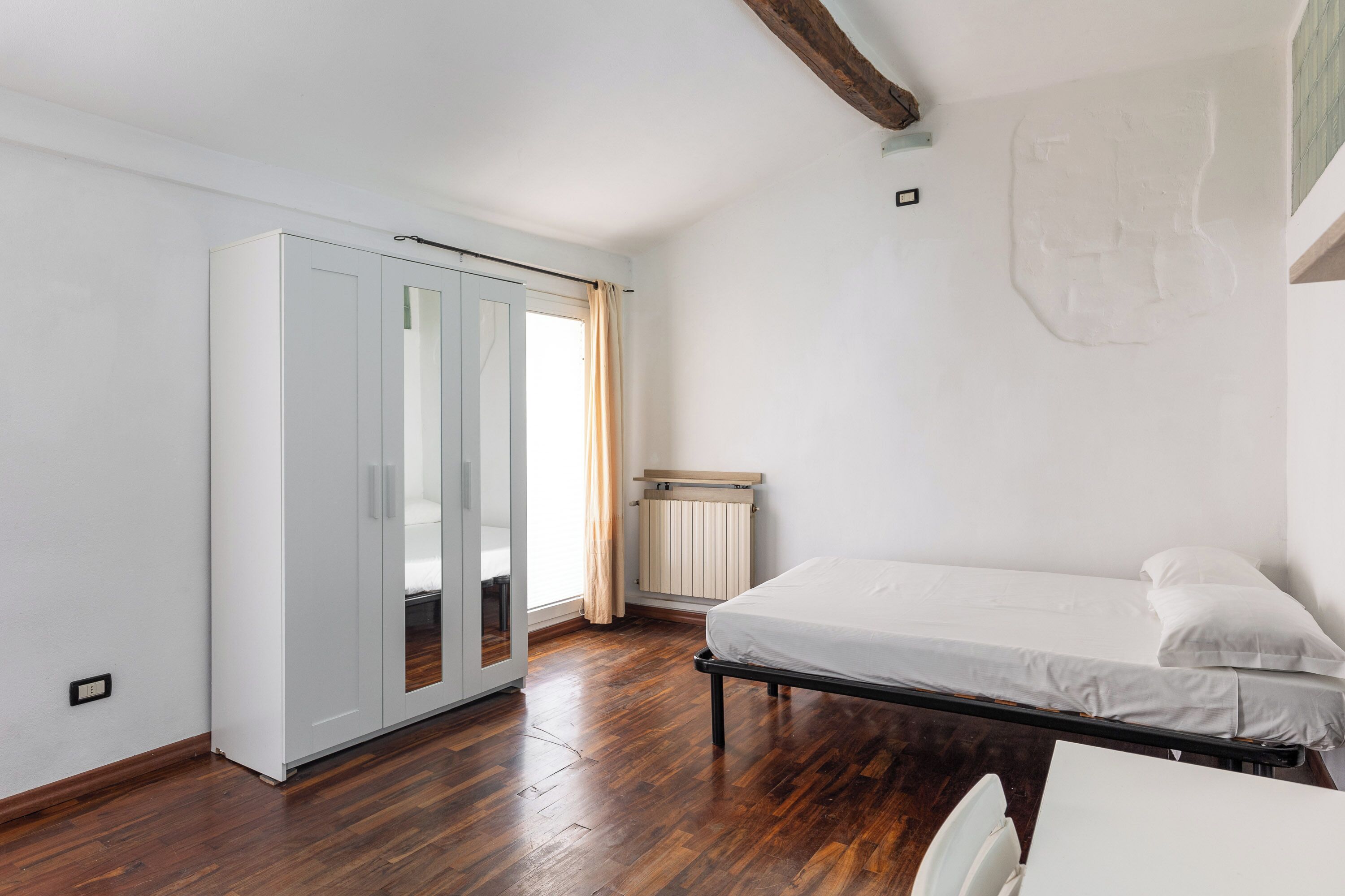 Une chambre à coucher avec un lit, une armoire, un radiateur et une fenêtre avec des rideaux.