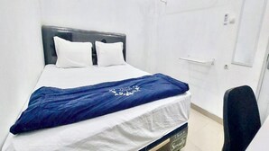 A single bed with a white and blue bedspread, a dark headboard, and a white wall with a door and a light switch. - OYO 94046 Tamansari Panoramic Apartment By Aw (Bandung)