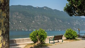 A bench by a lakeside path with a view of sailboats on the water and mountains in the background. - Appartement proche lac et commodités (Aix-les-Bains)