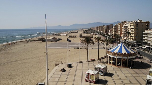 Una playa con un carrusel, palmeras y una vista despejada del mar y montañas al fondo.