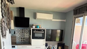 Un espacio habitable compacto con kitchenette, una cama con colcha rosa estampada y un sofá negro.