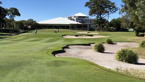 Um campo de golfe com bunkers e um edifício ao fundo.