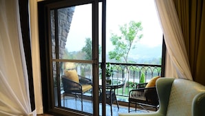Una habitación con un gran ventanal corredero que da a un patio exterior con mobiliario y vistas a la vegetación y montañas.