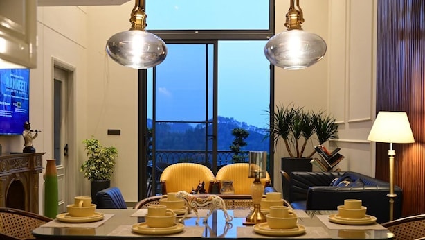Un comedor con una mesa dispuesta para cuatro, dos sillas, un sofá y un televisor al fondo.