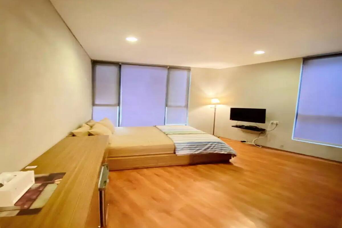 Een moderne slaapkamer met een houten vloer, een bed met een gestreept dekbed, een bureau met papieren, een lamp en een televisie aan de muur.