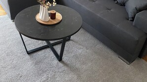 Una sala de estar moderna con un sofá seccional gris oscuro, una mesa de centro redonda negra con un jarrón de flores y una vela.