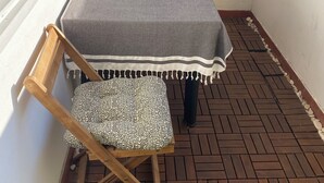 Un pequeño patio con una mesa, una silla, una ventana con mosquitero y piso de baldosas.