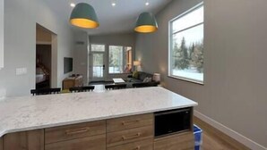 A modern kitchen with a large island, pendant lighting, and a view of a snowy landscape through a large window.