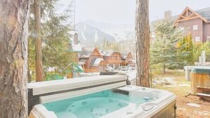 Een hottub met uitzicht op een bergachtig landschap en een houten chalet op de achtergrond.