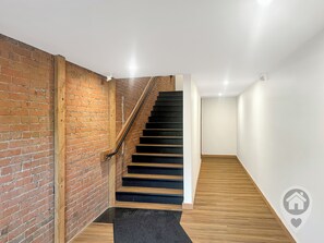 Eine Treppe mit Holzstufen und einem schwarzen Geländer, die zu einem Raum mit weißen Wänden und Holzboden führt.