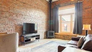 Ein Wohnzimmer mit Backsteinwand, Fernseher, einer Couch, einer Lampe und einem Fenster mit Vorhängen.