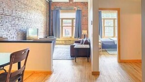 Ein moderner Wohnraum mit einer Ziegelwand, einem Essbereich mit Tisch und Stühlen, einer Couch und einem Fenster mit Vorhängen.