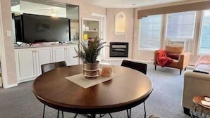 Un salon moderne avec une table de salle à manger ronde en bois, un téléviseur à écran plat fixé à un meuble et un ventilateur de plafond.
