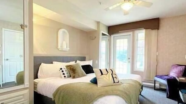 Une chambre à coucher avec un lit, un ventilateur de plafond, une fenêtre et une chaise.