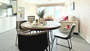 Un coin repas avec une table ronde, deux chaises, une plante en pot et une cuisine en arrière-plan.