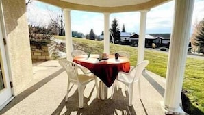Une terrasse couverte avec une table ronde et quatre chaises, une nappe rouge et une vue sur un quartier résidentiel.