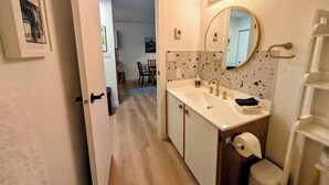 A bathroom with a white sink, a mirror with lights above it, and a towel rack.