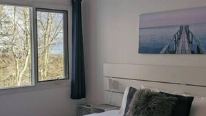 A bedroom with a bed, a window with a view of trees, and a painting on the wall.