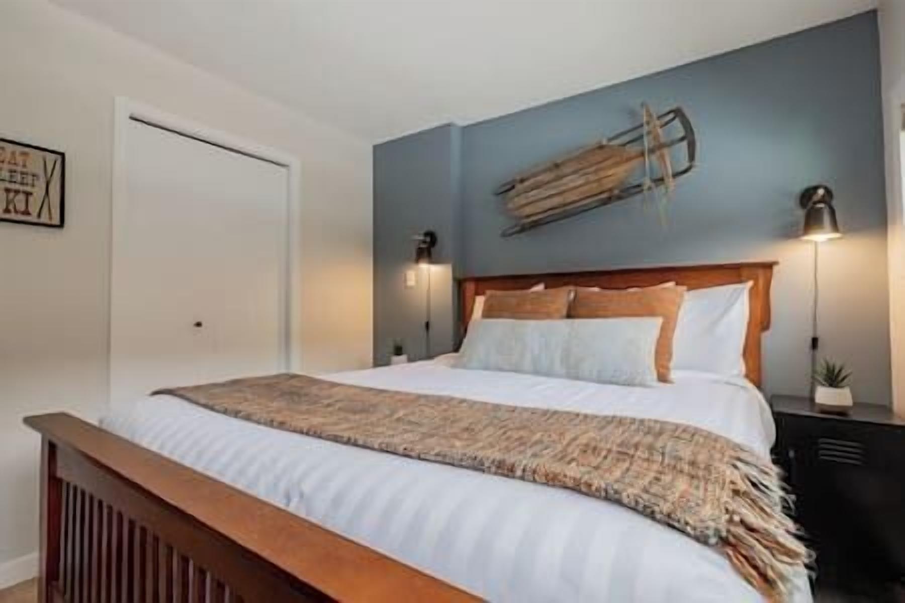 A neatly made bed with a wooden headboard, a bedside lamp, and a wall-mounted shelf above it.