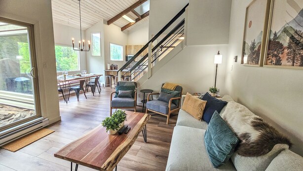 Uma sala de estar ampla com piso de madeira, um sofá com almofadas, uma mesa de centro e uma escada que leva a um andar superior.