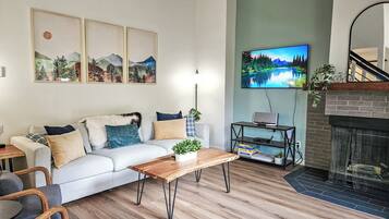 A modern living room with a sofa, coffee table, and TV. There are framed pictures on the wall and a fireplace.