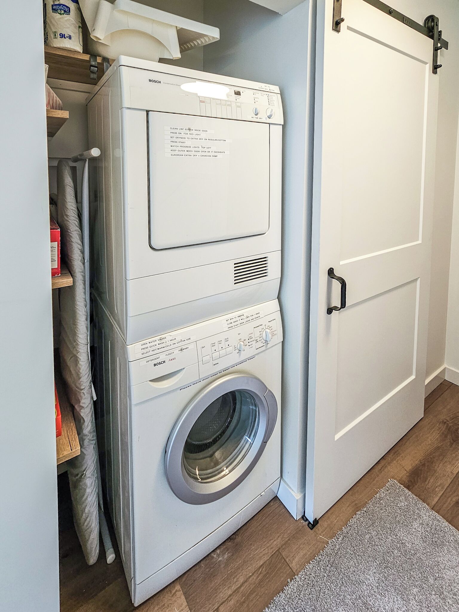 Un área de lavandería compacta con lavadora y secadora apiladas, una puerta blanca y piso de madera.