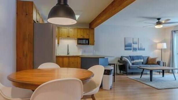 A modern kitchen with wooden cabinets, a dining area with a round table and chairs, and a living room with a sofa and a coffee table. - 3 Bed Townhouse - Fireplace - Great Location (Fernie)