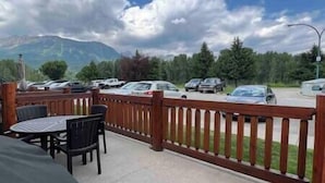 A covered outdoor seating area with tables and chairs, a wooden fence, and a view of parked cars and trees. - 3 BDRM Condo - Superb Location - Parking (Fernie)