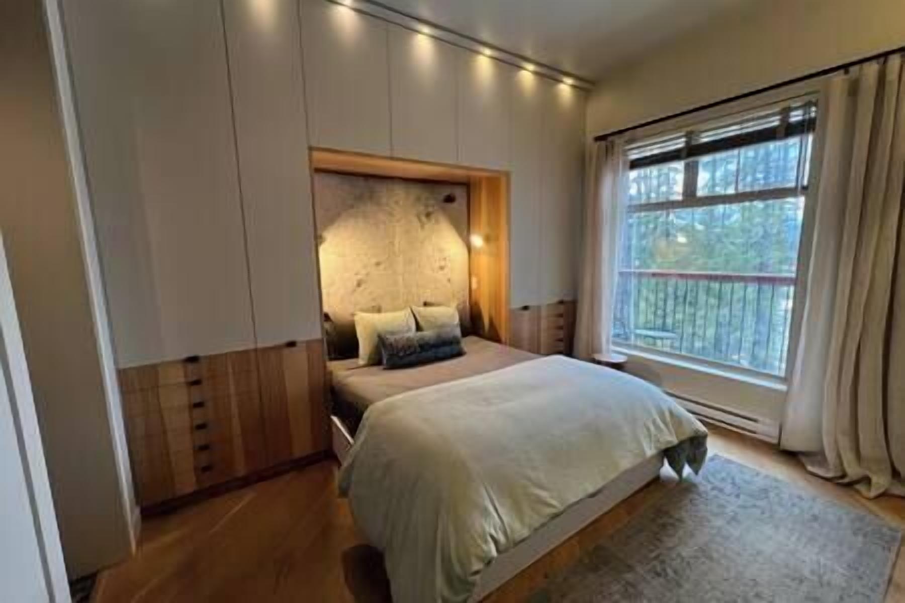 A bedroom with a bed, a headboard, a window, and a view of the outdoors.
