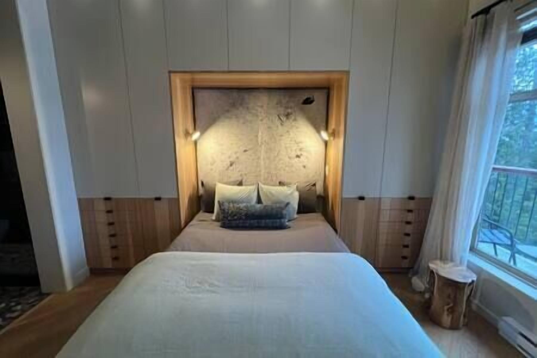 A bedroom with a large bed, a wooden headboard, and a view of the outdoors through a window.