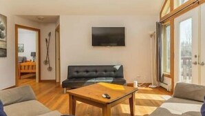 A living room with a black sofa, a wooden coffee table, and a television on the wall.