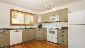A kitchen with wooden flooring, white appliances, and light green cabinets.