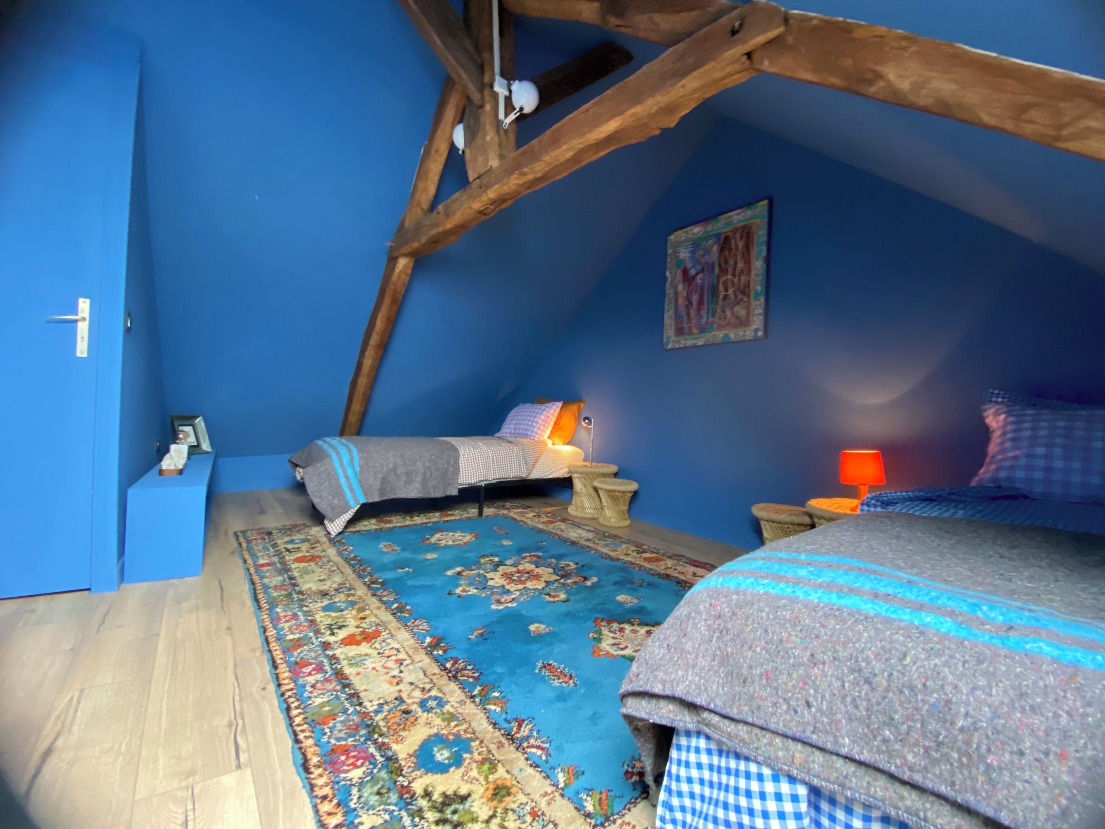 A bedroom with a sloped ceiling, a bed, a rug, and a nightstand with a lamp.