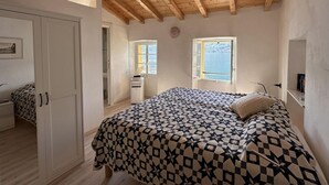Un dormitori amb sostre de fusta, un llit amb llençols estampats, un armari i una finestra amb vista al mar.